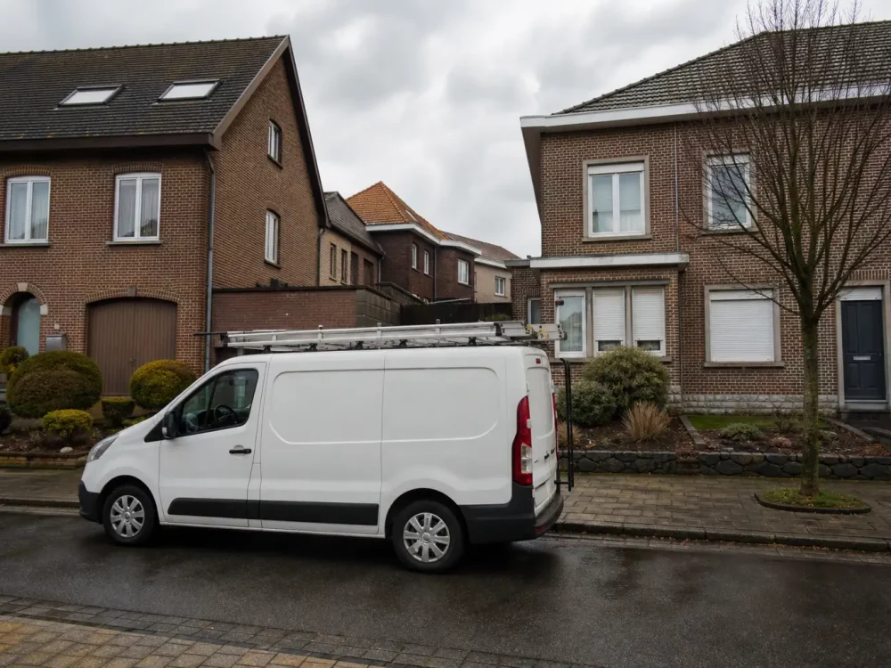 Camionnette blanche d'un installateur devant des maisons en briques en Belgique.