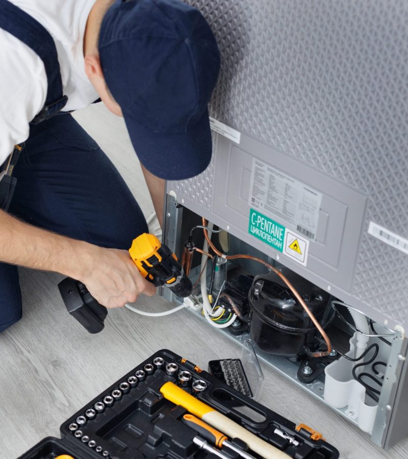Male technician repairs a refrigerator in the kitchen in close-up