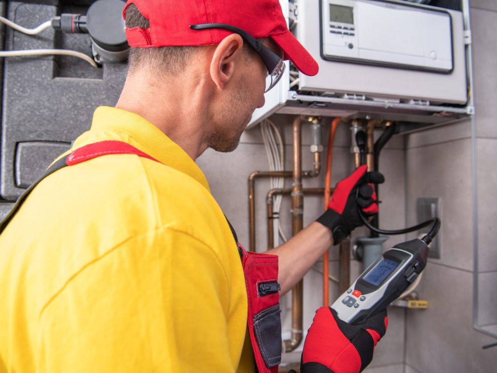 A technician in a yellow shirt and red gloves inspects and tests a heating system in a residential space, ensuring proper operation and safety.